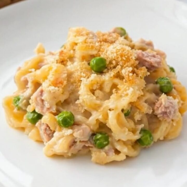 A creamy portion of tuna casserole with egg noodles, sweet peas, and a golden panko crust on a white plate