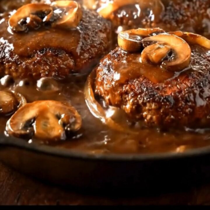 A cast-iron skillet filled with juicy hamburger steaks covered in a rich, dark mushroom gravy.