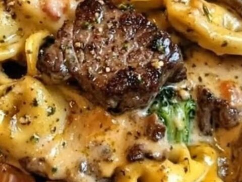 Skillet filled with creamy garlic parmesan tortellini, seared steak bites, and broccoli.