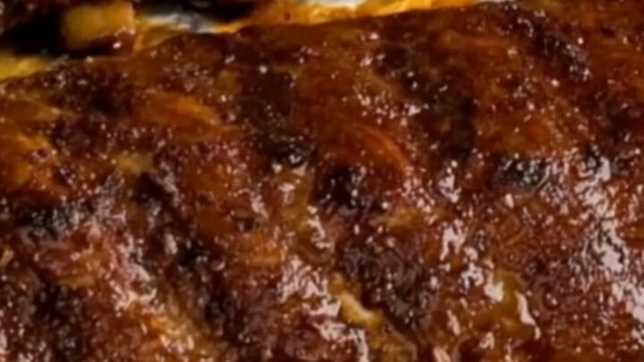 Sticky, caramelized oven-baked BBQ pork ribs arranged on a white serving plate with a glossy finish.