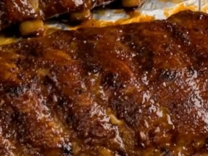 Sticky, caramelized oven-baked BBQ pork ribs arranged on a white serving plate with a glossy finish.