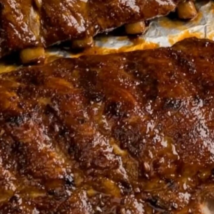 Sticky, caramelized oven-baked BBQ pork ribs arranged on a white serving plate with a glossy finish.