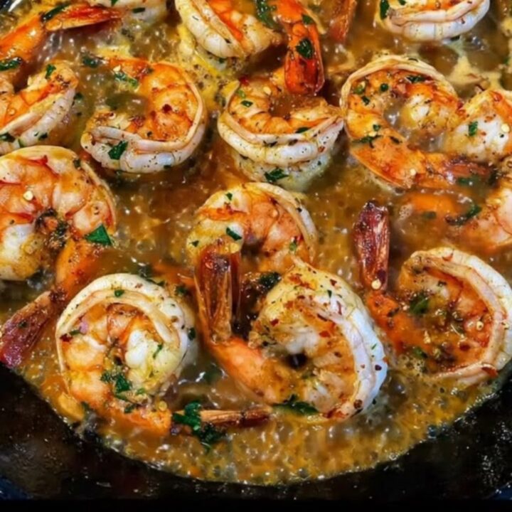 A cast-iron skillet filled with plump, pink shrimp coated in a glossy, golden garlic butter sauce with chili flakes.