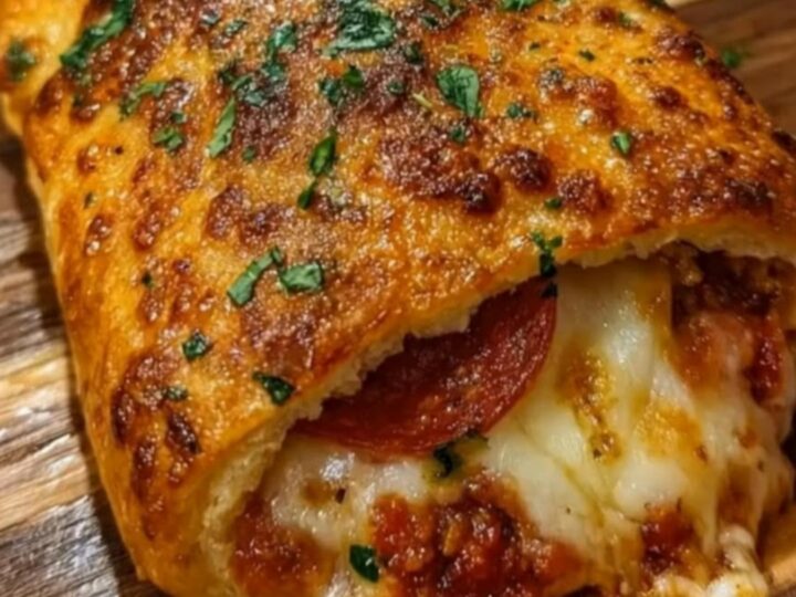 A golden-baked stromboli resting on a wooden cutting board with a slice being lifted to show a cheese pull.