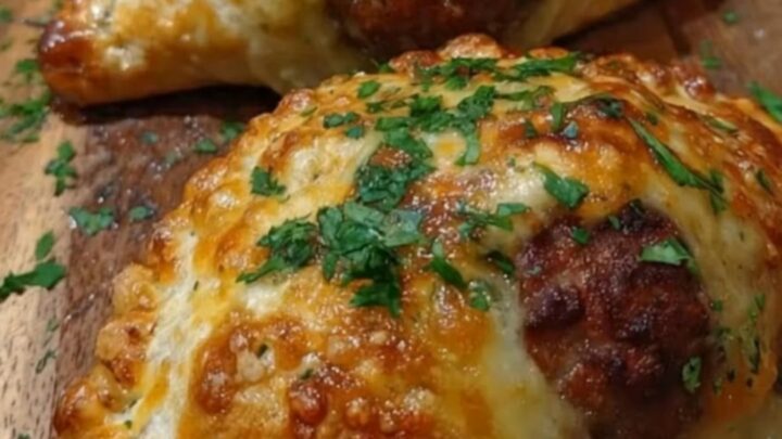A wooden board holding several golden-brown meatball pockets topped with fresh green parsley.