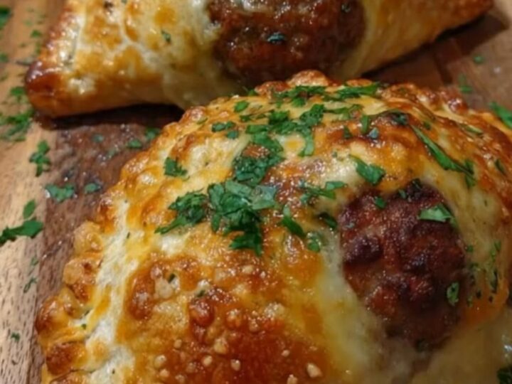 A wooden board holding several golden-brown meatball pockets topped with fresh green parsley.