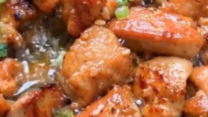 A close-up of golden-brown garlic butter chicken bites in a skillet topped with fresh green onions and parsley.