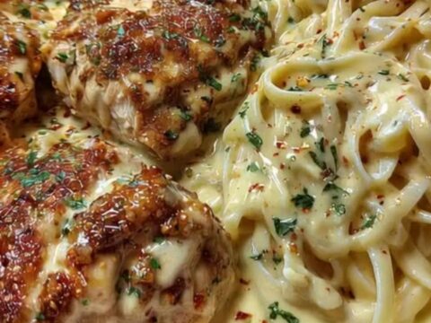 A plate of creamy Cajun Alfredo pasta alongside sliced golden-brown chicken cutlets garnished with herbs