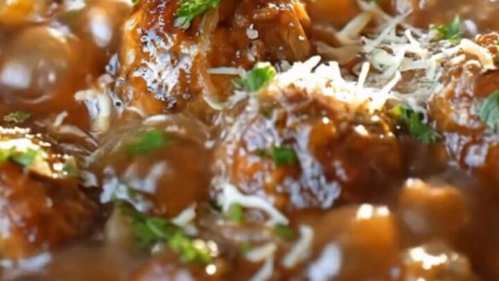 A close-up of tender meatballs in a rich onion gravy topped with melted swiss cheese in a slow cooker.
