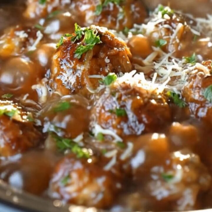 A close-up of tender meatballs in a rich onion gravy topped with melted swiss cheese in a slow cooker.