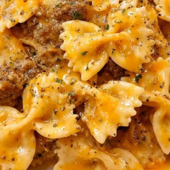 A close-up shot of creamy garlic butter beef bowtie pasta served in a white bowl, showing melted cheddar cheese.