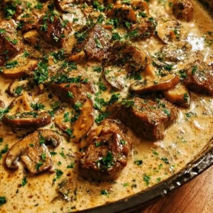 A steaming creamy beef and mushroom skillet served in a rustic pan with fresh parsley.