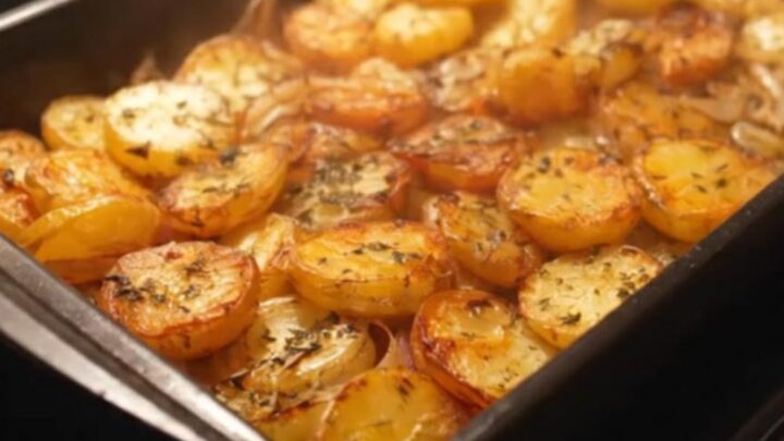 A golden, crispy roasted potato and onion dish served on a white plate.