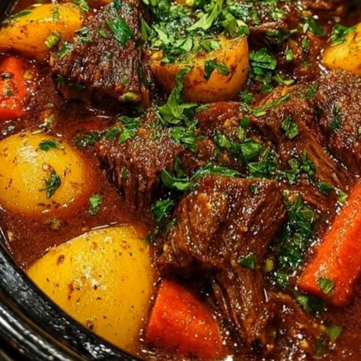 A steaming, glossy portion of beef stew with tender chunks of beef, carrots, and potatoes in a white bowl.
