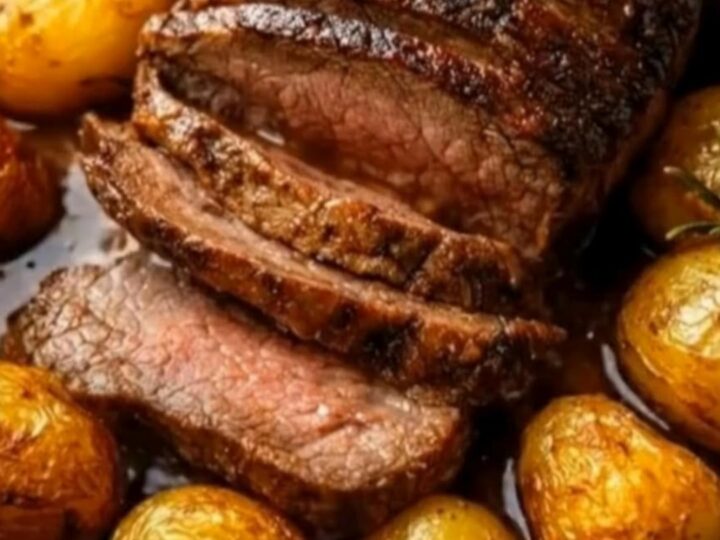 A beautifully roasted beef with golden baby potatoes in an oval pan, showing a juicy, tender slice.