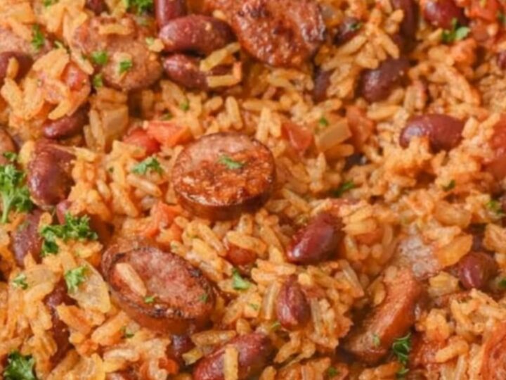 A steaming plate of Cajun red beans and rice with slices of browned sausage.