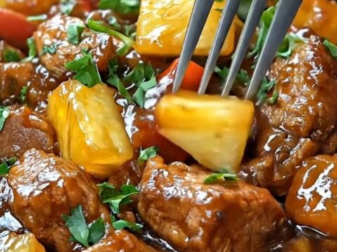 A close-up of tender hoisin pork chunks and pineapple in a black slow cooker with steam rising.