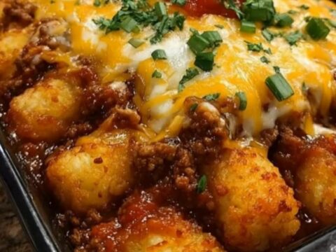 A steaming, golden-brown Sloppy Joe Tater Tot Casserole in a black baking dish with melted cheese and green onions.