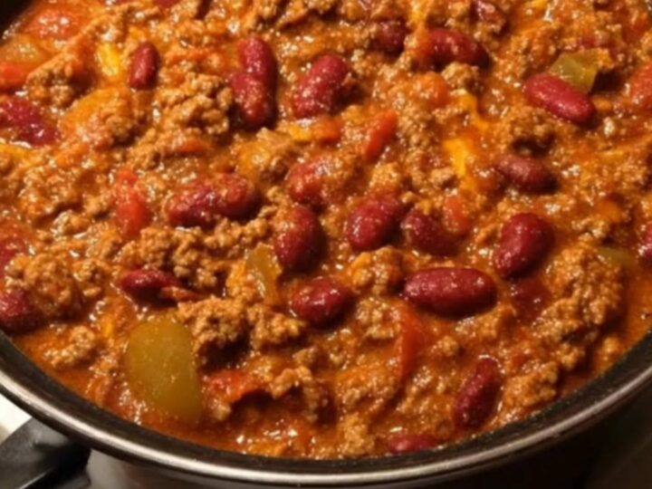 A steaming white bowl filled with hearty beef and kidney bean chili, viewed from above in a cozy kitchen setting.