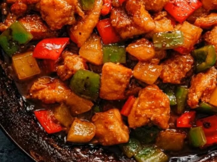 A glossy pineapple chicken stir-fry with bell peppers in a rustic black skillet.