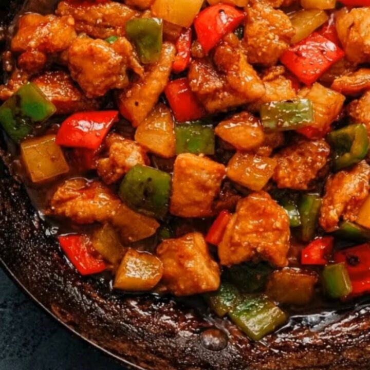 A glossy pineapple chicken stir-fry with bell peppers in a rustic black skillet.