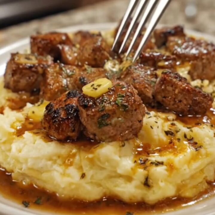Juicy garlic butter steak bites served over a bed of creamy mashed potatoes in a cast-iron skillet.