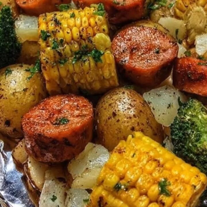 A steaming garlic butter sausage and potato foil packet opened to reveal roasted sausage, baby potatoes, corn, and broccoli.