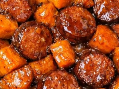 A steaming, hearty portion of sliced smoked sausage and tender sweet potato chunks in a rich, sticky glaze.