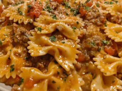 A close-up view of creamy bowtie pasta coated in a rich beef and tomato sauce, garnished with fresh green parsley.