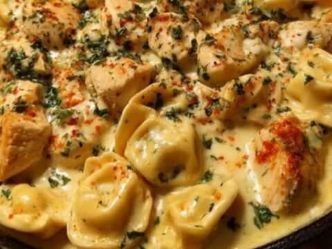 A close-up of a creamy chicken tortellini skillet in a black cast-iron pan with fresh herbs.