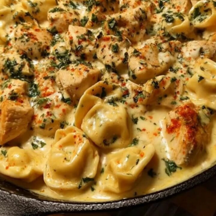 A close-up of a creamy chicken tortellini skillet in a black cast-iron pan with fresh herbs.