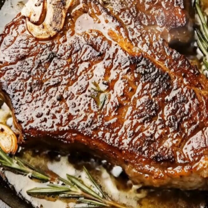 A perfectly seared T-bone steak with a golden brown crust, topped with melting garlic butter and fresh rosemary sprigs.