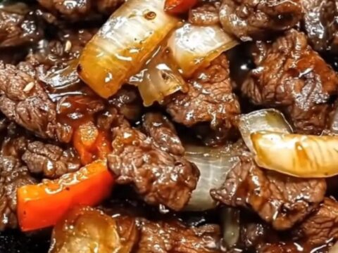 A steaming cast-iron skillet filled with glossy beef strips, caramelized onions, and colorful bell peppers.