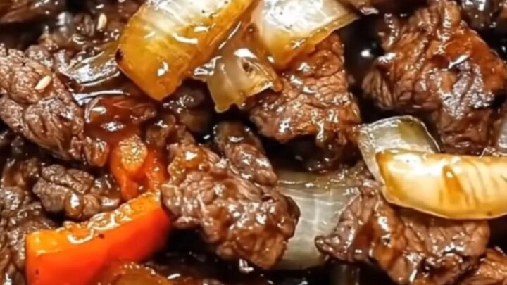 A steaming cast-iron skillet filled with glossy beef strips, caramelized onions, and colorful bell peppers.