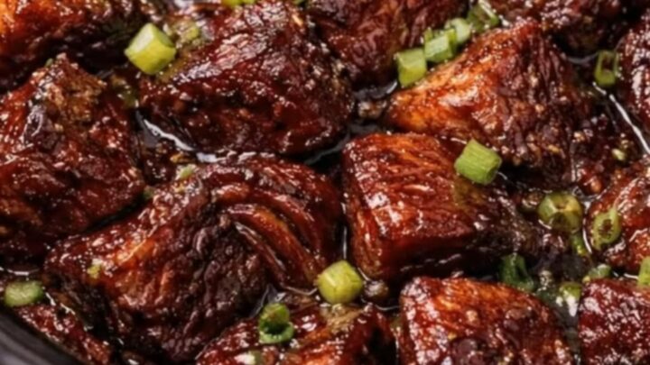Close up of sticky BBQ burnt ends in a black slow cooker with steam rising.