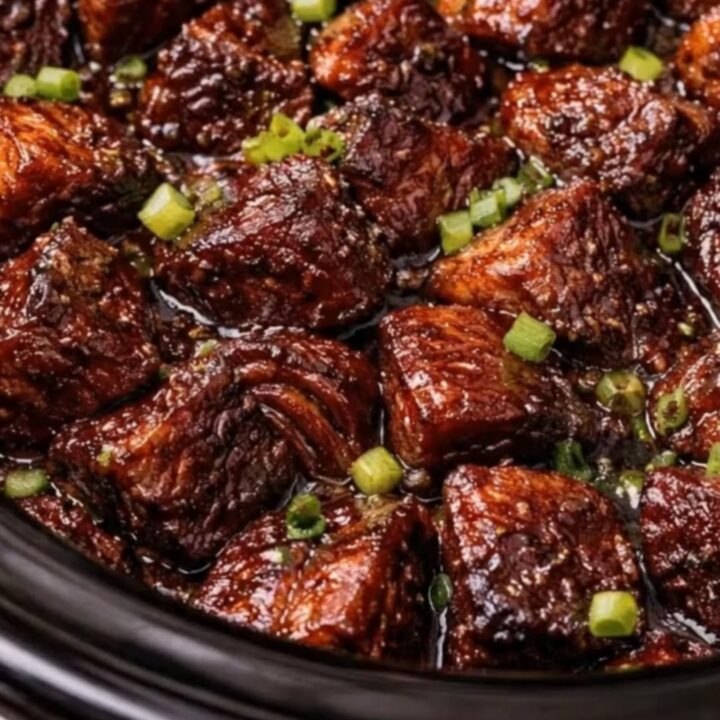 Close up of sticky BBQ burnt ends in a black slow cooker with steam rising.