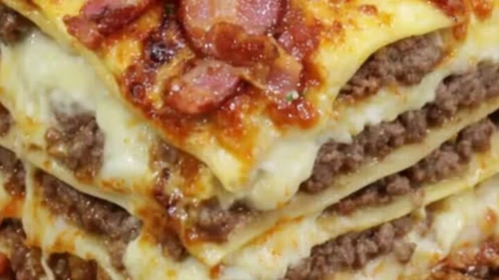 A thick square slice of Parmesan garlic bacon cheeseburger lasagna resting on a rustic wooden board.