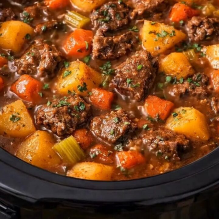 A close-up of a black slow cooker filled with hearty beef stew, featuring visible chunks of beef, carrots, and potatoes.