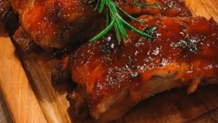 A close-up of glossy, caramelized sticky honey garlic ribs next to a heap of creamy mashed potatoes on a wooden board.