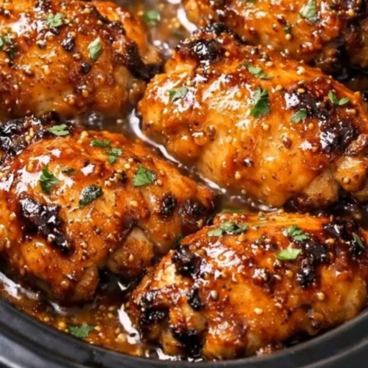 A glossy, caramelized chicken thigh served on a white plate with visible steam rising from the tender meat.