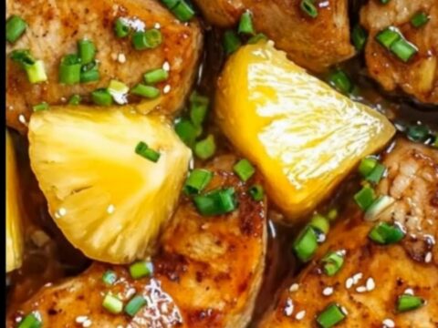 A juicy pork chop topped with pineapple chunks and green onions, served on a white plate with steamed rice.