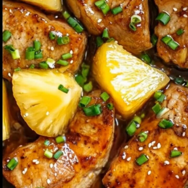 A juicy pork chop topped with pineapple chunks and green onions, served on a white plate with steamed rice.