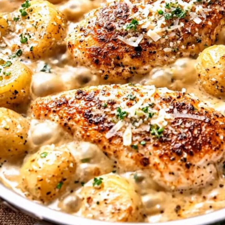 Creamy garlic parmesan chicken with tender baby potatoes in a stainless steel skillet.