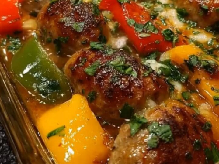 A glass dish filled with browned Italian sausage meatballs and colorful sliced bell peppers.