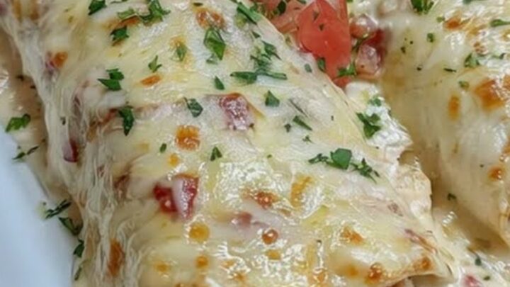 A white rectangular platter holding two golden, cheese-blanketed chicken enchiladas topped with fresh diced tomatoes
