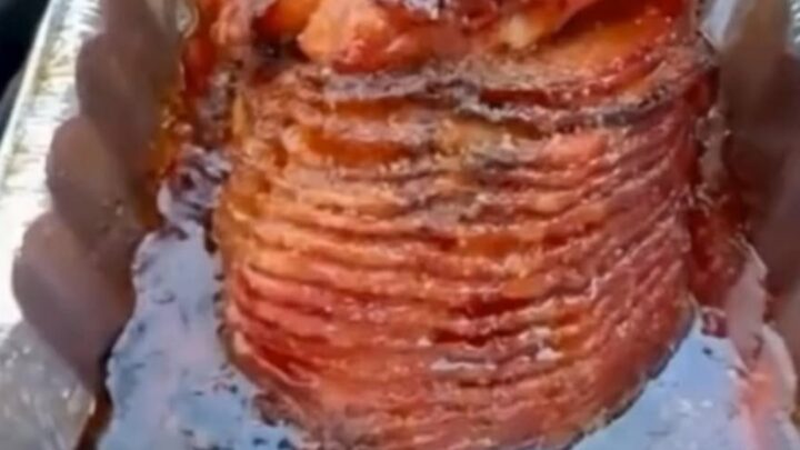 A glossy, caramelized spiral-cut ham glistening in an aluminum pan with a rich bourbon brown sugar glaze.