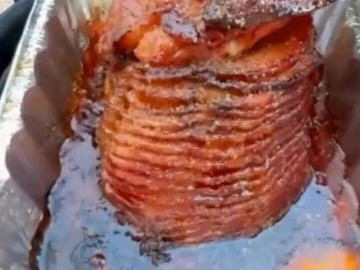A glossy, caramelized spiral-cut ham glistening in an aluminum pan with a rich bourbon brown sugar glaze.