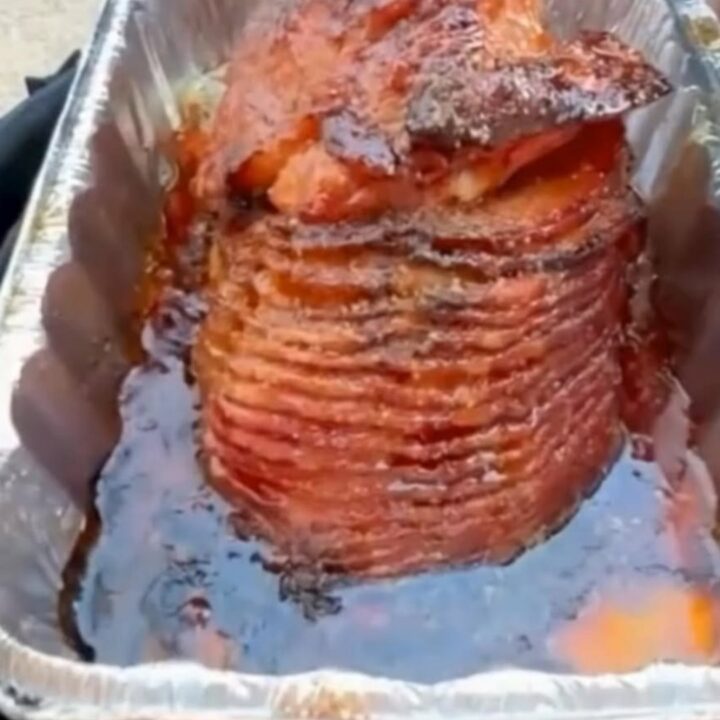 A glossy, caramelized spiral-cut ham glistening in an aluminum pan with a rich bourbon brown sugar glaze.