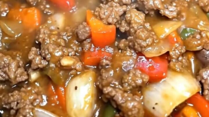 A close-up of a slow cooker filled with tender beef, bell peppers, and onions in a rich brown gravy.