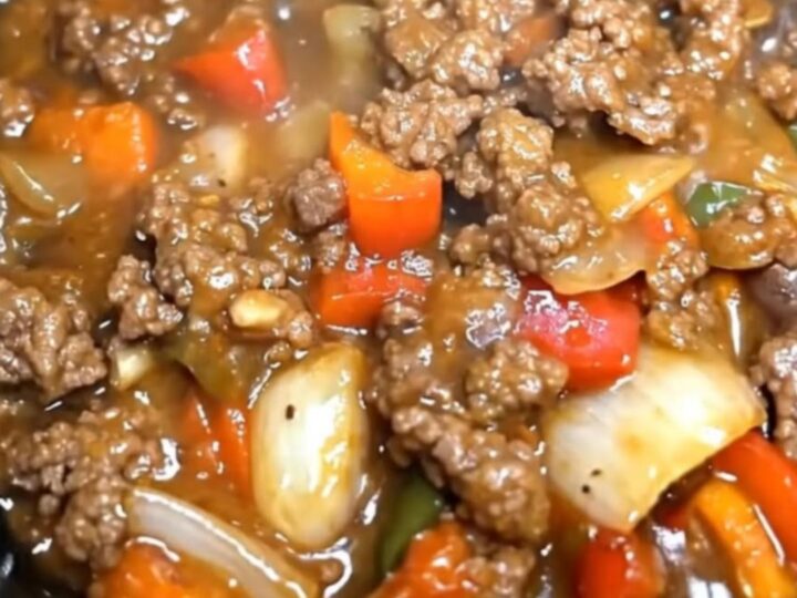 A close-up of a slow cooker filled with tender beef, bell peppers, and onions in a rich brown gravy.